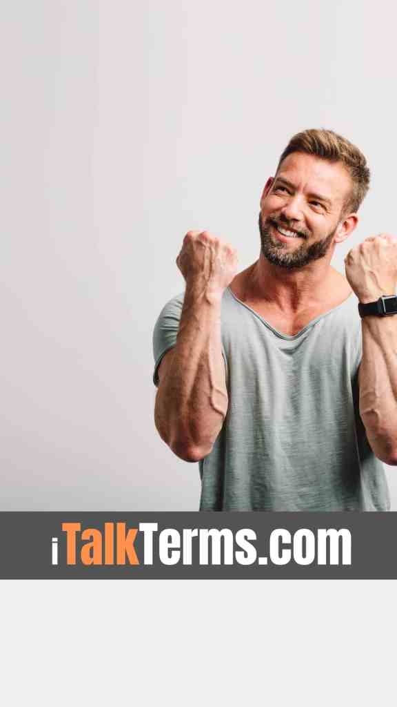 A smiling man expressing excitement with clenched fists, wearing a grey t-shirt, against a light background.